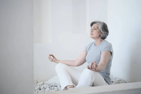 Een bejaarde fitte vrouw die yoga en meditatie beoefent in een poging harmonie en evenwicht te bereiken — Stockfoto