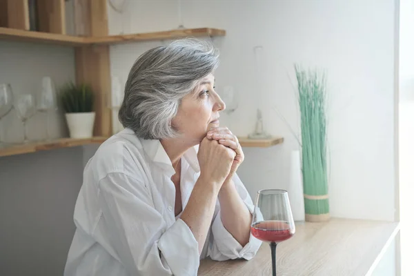 Senior woman enjoys a glass of red wine and remembering pleasant moments and thinking about pleasant things