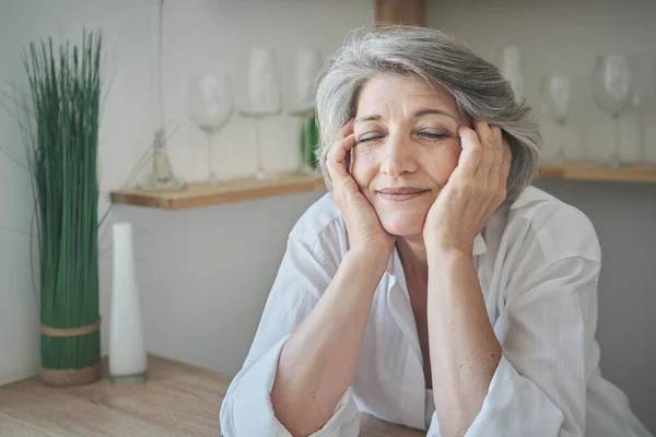 Retrato de una anciana mayor feliz con los ojos cerrados en un apartamento luminoso y confortable. — Foto de Stock