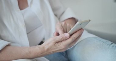 Akıllı telefon kullanan yaşlı, orta yaşlı bir kadının yakın çekimi.,