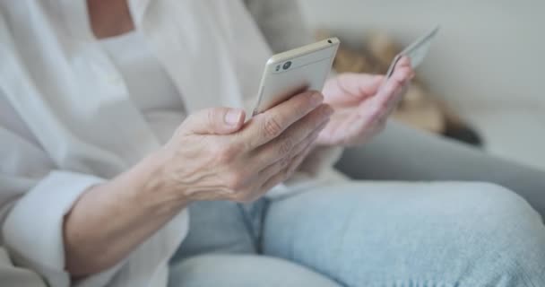 Close-up van een oudere vrouw die een creditcard en een mobiele telefoon gebruikt om online te kopen. — Stockvideo