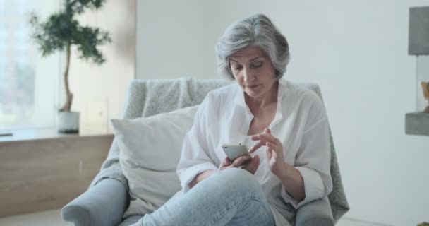 Vecchia donna di mezza età che guarda lo schermo dello smartphone guardando foto o video divertenti — Video Stock