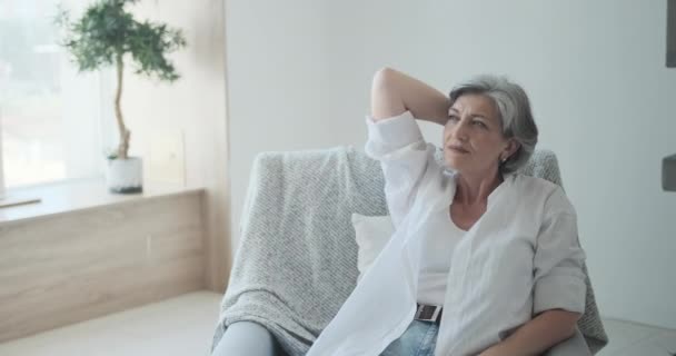 Ältere Dame lehnt sich auf bequemem Stuhl zurück, fröhliche ältere Dame im Wohnzimmer — Stockvideo