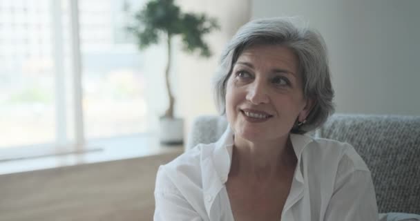 Glücklich attraktive ältere erwachsene Dame starrt in die Kamera sitzt allein auf dem Sofa zu Hause — Stockvideo