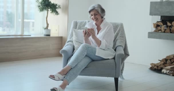 Seniorin schaut auf Smartphone-Bildschirm und sieht lustiges Foto oder Video — Stockvideo