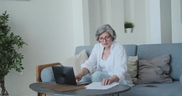 Ältere Geschäftsfrau mit konzentriertem Gesichtsausdruck hält eine Haushaltszeitung mit kommerziellen Informationen in der Hand — Stockvideo