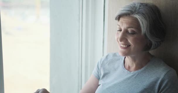 Una donna anziana sorride alla finestra e aspetta i suoi figli — Video Stock