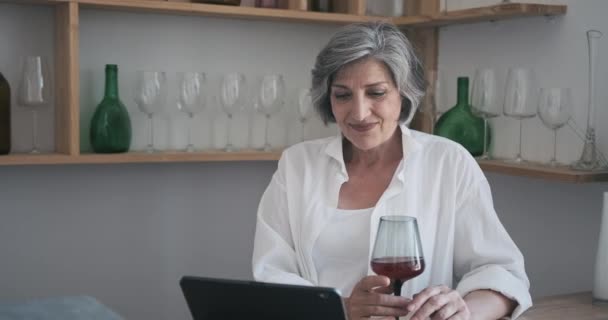 Gammal äldre 60-årig kvinna som står med en surfplatta, dricker vin och njuter av videosamtal — Stockvideo