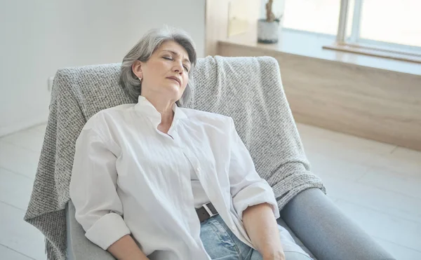 Relajante mujer mayor sonriente sentada en una silla acogedora, estiramiento, relajante, — Foto de Stock