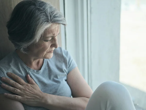 Oudere oudere zieke gehandicapte, verdrietige vrouw in pijn en lijden zittend bij het raam in het ziekenhuis. — Stockfoto