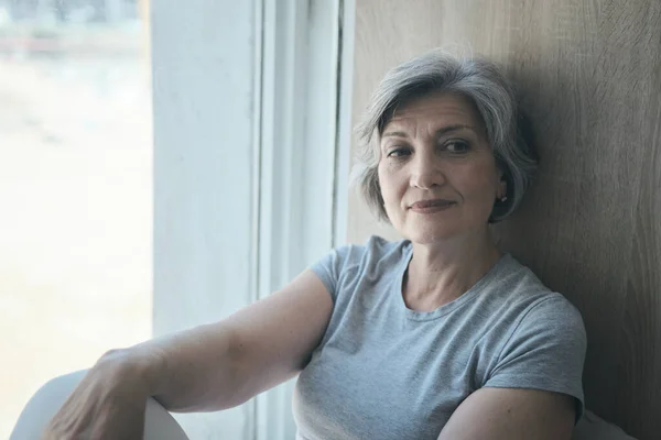 An elderly woman smiling at the window and waiting for her children