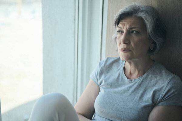 Elderly senior sick disabled, sad woman in pain and suffering sitting by the window in the hospital.