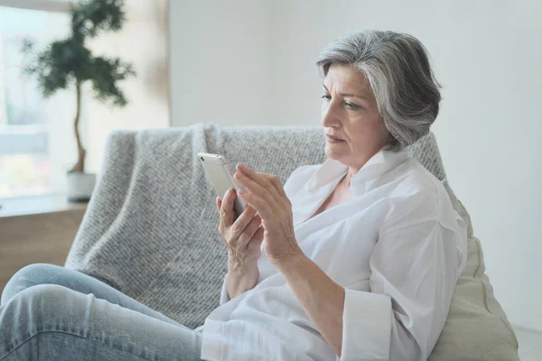 Móvil adicto senior mujer madura uso de teléfono inteligente todo el tiempo en casa — Foto de Stock