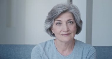 Evdeki kanepede oturan gündelik elbiseli güzel ve zeki büyükannenin yakın çekimi.