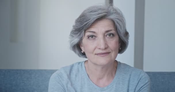 Крупный план красивой интеллигентной бабушки в повседневной одежде дома, сидящей на диване — стоковое видео