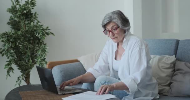 An elderly woman lawyer or accountant in eyeglasses working from home with a computer and documents — Stock Video