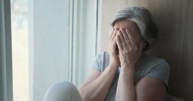 Üzgün yaşlı kadın pencereden dışarı bakıyor, yaşlılığında yapayalnız..