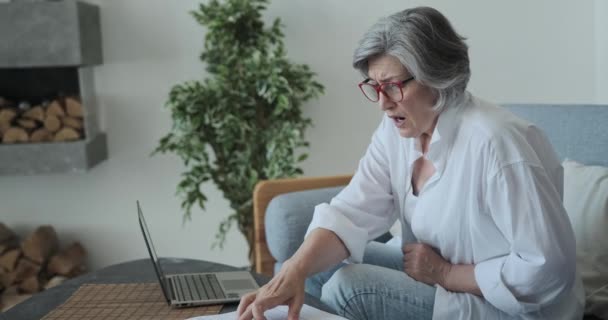 Oudere volwassen oude serieuze vrouw werken met laptop en papier, geschokt door hoge belastingen en pensioensparen problemen — Stockvideo