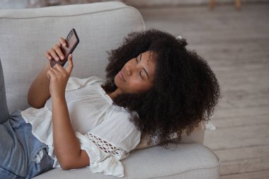 Sosyal ağda iletişim kuran cep telefonu uygulamaları kullanan rahat, genç bir ırk kadını.