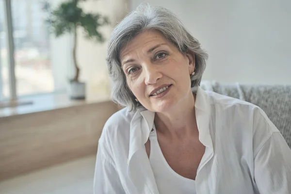 Portret van een vrolijke oudere vrouw in een licht comfortabel appartement. — Stockfoto