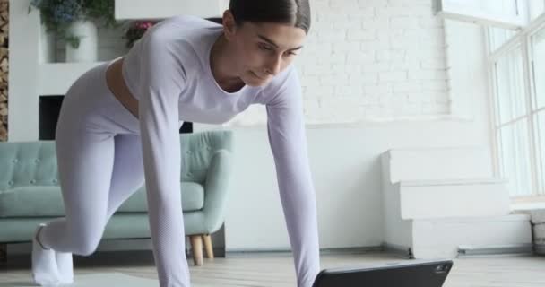 Brunette with long ponytail looks at tablet display and practices exercise — Stock Video