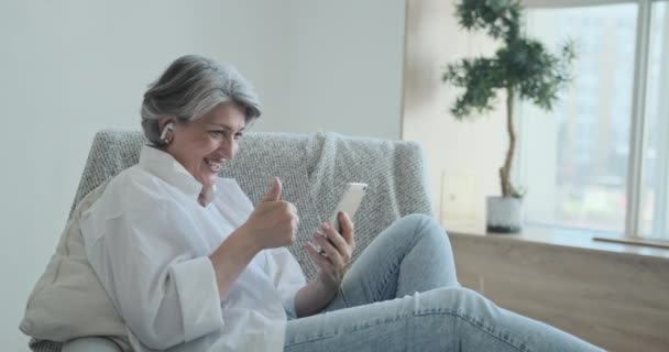 Glückliche Seniorin blickt auf Handy, winkt und grüßt. — Stockvideo