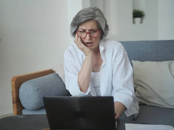 Oudere volwassen oude serieuze vrouw werken met laptop en papier, geschokt door hoge belastingen en pensioensparen problemen — Stockfoto