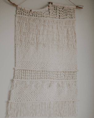 Boho tarzı duvar paneli, makrome tekniğini kullanarak doğal beyaz ipliklerden yapılmış. Ev dekorasyonu ve düğün dekorasyonu. El yapımı doğal pamuk makrome dekorasyonu beyaz duvarda asılı..