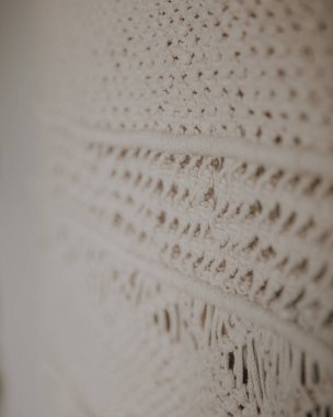 Boho tarzı duvar paneli, makrome tekniğini kullanarak doğal beyaz ipliklerden yapılmış. Ev dekorasyonu ve düğün dekorasyonu. El yapımı doğal pamuk makrome dekorasyonu beyaz duvarda asılı..