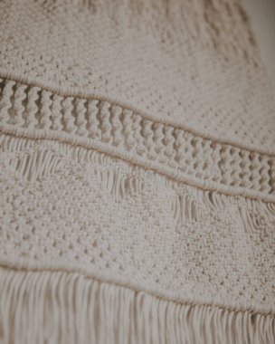 Boho tarzı duvar paneli, makrome tekniğini kullanarak doğal beyaz ipliklerden yapılmış. Ev dekorasyonu ve düğün dekorasyonu. El yapımı doğal pamuk makrome dekorasyonu beyaz duvarda asılı..