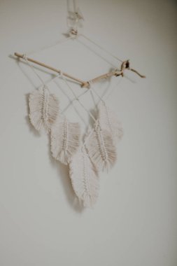 Boho tarzı duvar paneli, makrome tekniğini kullanarak doğal beyaz ipliklerden yapılmış. Ev dekorasyonu ve düğün dekorasyonu. El yapımı doğal pamuk makrome dekorasyonu beyaz duvarda asılı..