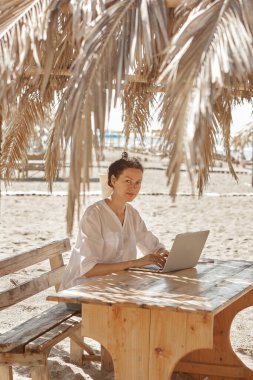 Kumsalda dizüstü bilgisayar kullanan genç bir kadın. Serbest çalışma kavramı