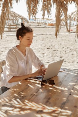 Kumsalda dizüstü bilgisayar kullanan genç bir kadın. Serbest çalışma kavramı