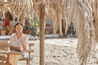 Kumsalda dizüstü bilgisayar kullanan genç bir kadın. Serbest çalışma kavramı