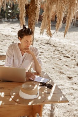 Kumsalda dizüstü bilgisayar kullanan genç bir kadın. Serbest çalışma kavramı