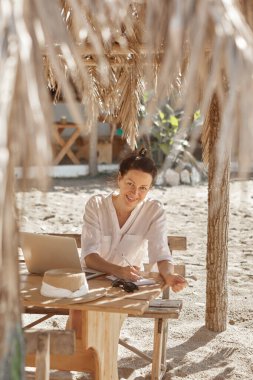 Kumsalda dizüstü bilgisayar kullanan genç bir kadın. Serbest çalışma kavramı