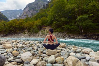 Doğada yoga dersleri. Tek başına spor yapma kavramı. Sosyal dışlama. Bir kadın kayalıklarda yoga yapıyor, bir dağ nehrinin yanında.