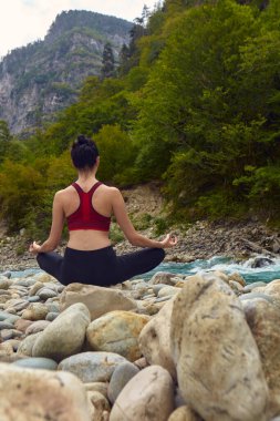 Doğada yoga dersleri. Tek başına spor yapma kavramı. Sosyal dışlama. Bir kadın kayalıklarda yoga yapıyor, bir dağ nehrinin yanında.