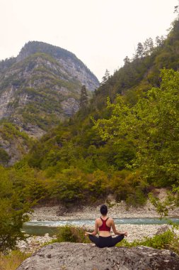 Doğada yoga dersleri. Tek başına spor yapma kavramı. Sosyal dışlama. Bir kadın kayalıklarda yoga yapıyor, bir dağ nehrinin yanında.