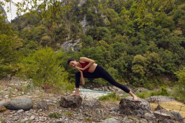 Doğada yoga dersleri. Tek başına spor yapma kavramı. Sosyal dışlama. Bir kadın kayalıklarda yoga yapıyor, bir dağ nehrinin yanında.