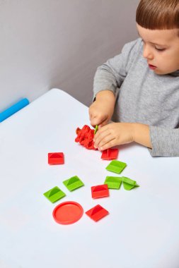 Oğlan odasında oyun oynuyor. Küçük çocuk oyun mu oynuyordu yoksa hamur mu oynuyordu? Çocuklar için eğitici oyuncaklar. Çocuk Gelişimi Oyunları. Çocuğun elleri kil yoğuruyor..