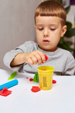 Oğlan odasında oyun oynuyor. Küçük çocuk oyun mu oynuyordu yoksa hamur mu oynuyordu? Çocuklar için eğitici oyuncaklar. Çocuk Gelişimi Oyunları. Çocuğun elleri kil yoğuruyor..