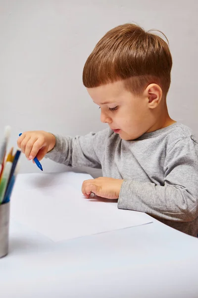 ブロンドの髪のかわいい男の子は自宅で色鉛筆を描きます 白いテーブルに描画します — ストック写真