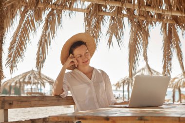 Kumsalda dizüstü bilgisayar kullanan genç bir kadın. Serbest çalışma kavramı