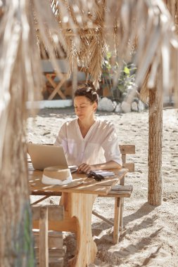 Kumsalda dizüstü bilgisayar kullanan genç bir kadın. Serbest çalışma kavramı