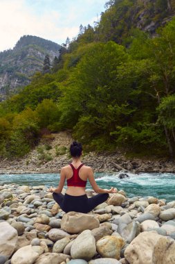 Doğada yoga dersleri. Tek başına spor yapma kavramı. Sosyal dışlama. Bir kadın kayalıklarda yoga yapıyor, bir dağ nehrinin yanında.