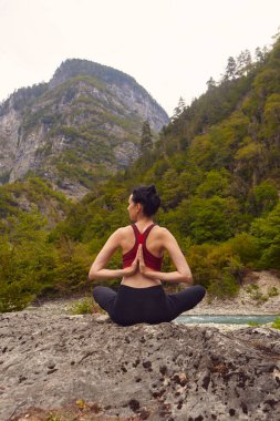 Doğada yoga dersleri. Tek başına spor yapma kavramı. Sosyal dışlama. Bir kadın kayalıklarda yoga yapıyor, bir dağ nehrinin yanında.
