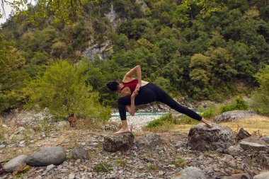 Doğada yoga dersleri. Tek başına spor yapma kavramı. Sosyal dışlama. Bir kadın kayalıklarda yoga yapıyor, bir dağ nehrinin yanında.