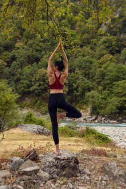 Doğada yoga dersleri. Tek başına spor yapma kavramı. Sosyal dışlama. Bir kadın kayalıklarda yoga yapıyor, bir dağ nehrinin yanında.