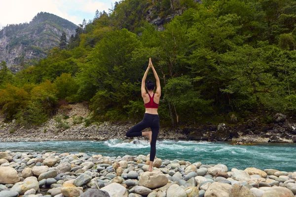 Doğada yoga dersleri. Tek başına spor yapma kavramı. Sosyal dışlama. Bir kadın kayalıklarda yoga yapıyor, bir dağ nehrinin yanında.